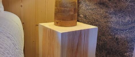 Una mesita de noche de madera con una lámpara, pared con textura y suelo de madera.