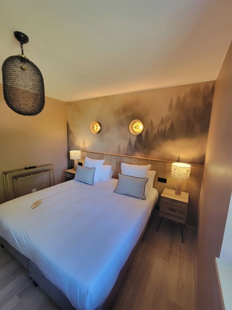 Une chambre d’hôtel avec un grand lit, deux tables de chevet avec des lampes, un luminaire fixé au mur et un plafonnier à motifs.
