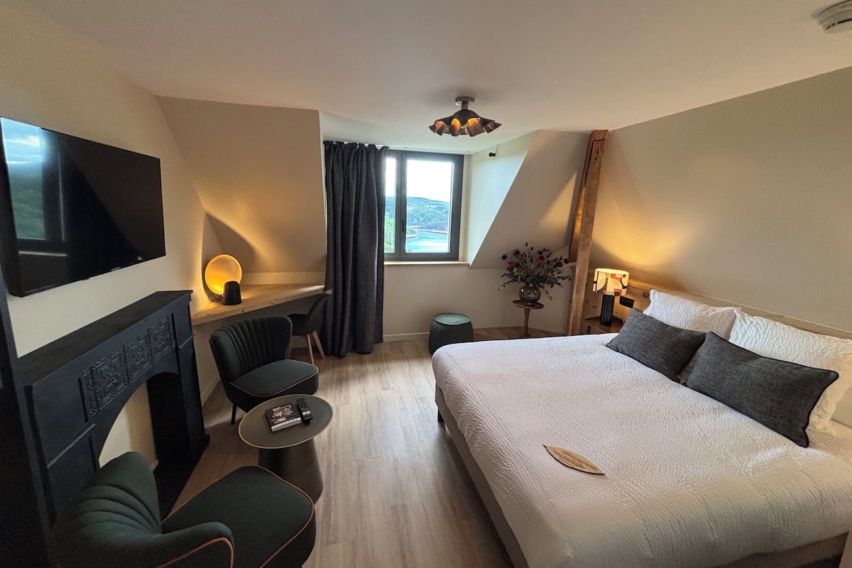 A hotel room with a bed, a desk, a chair, a TV, a fireplace, and a window with curtains.