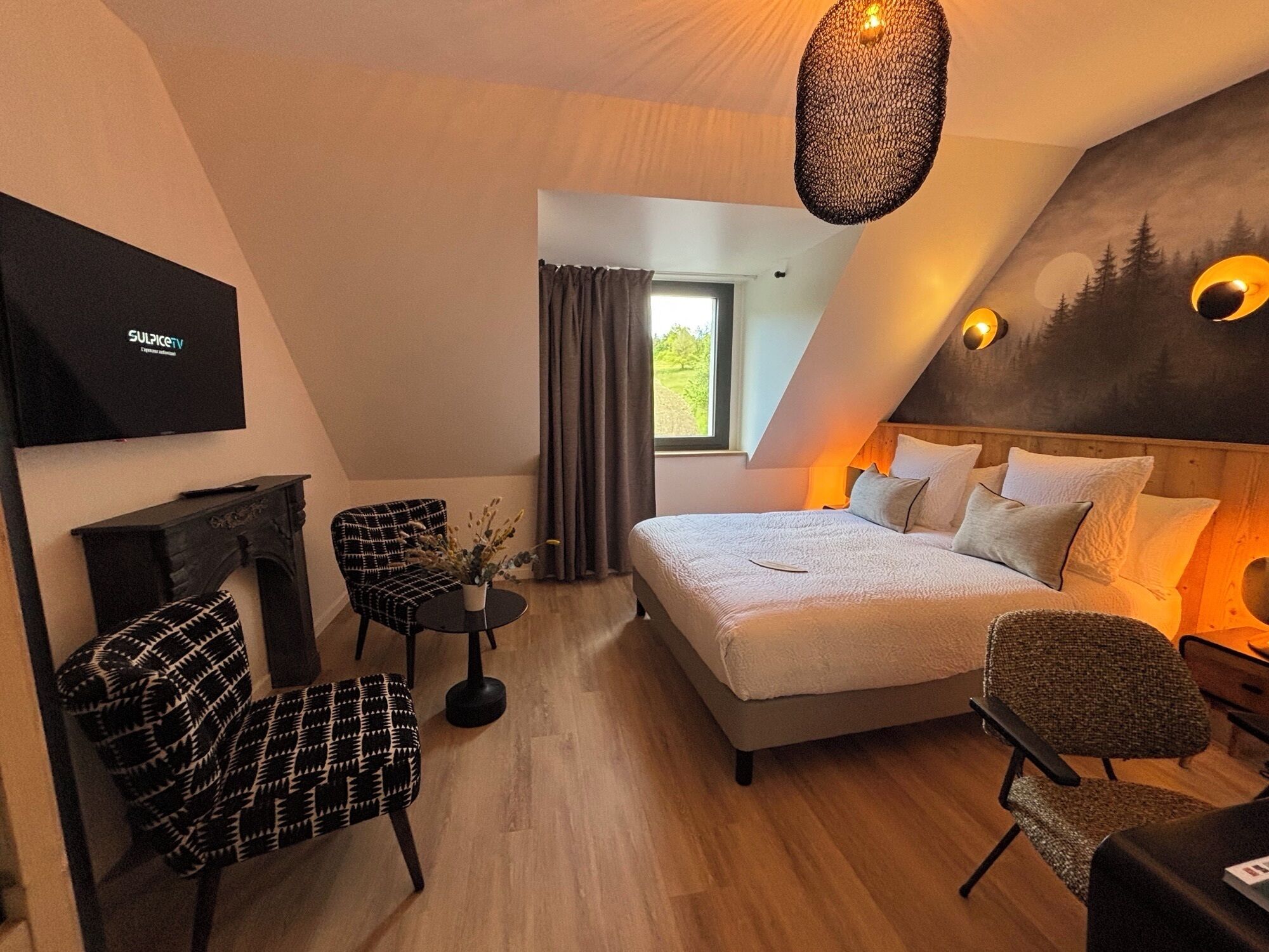 Un dormitorio moderno con cama, dos sillones, una mesita, chimenea y televisor.