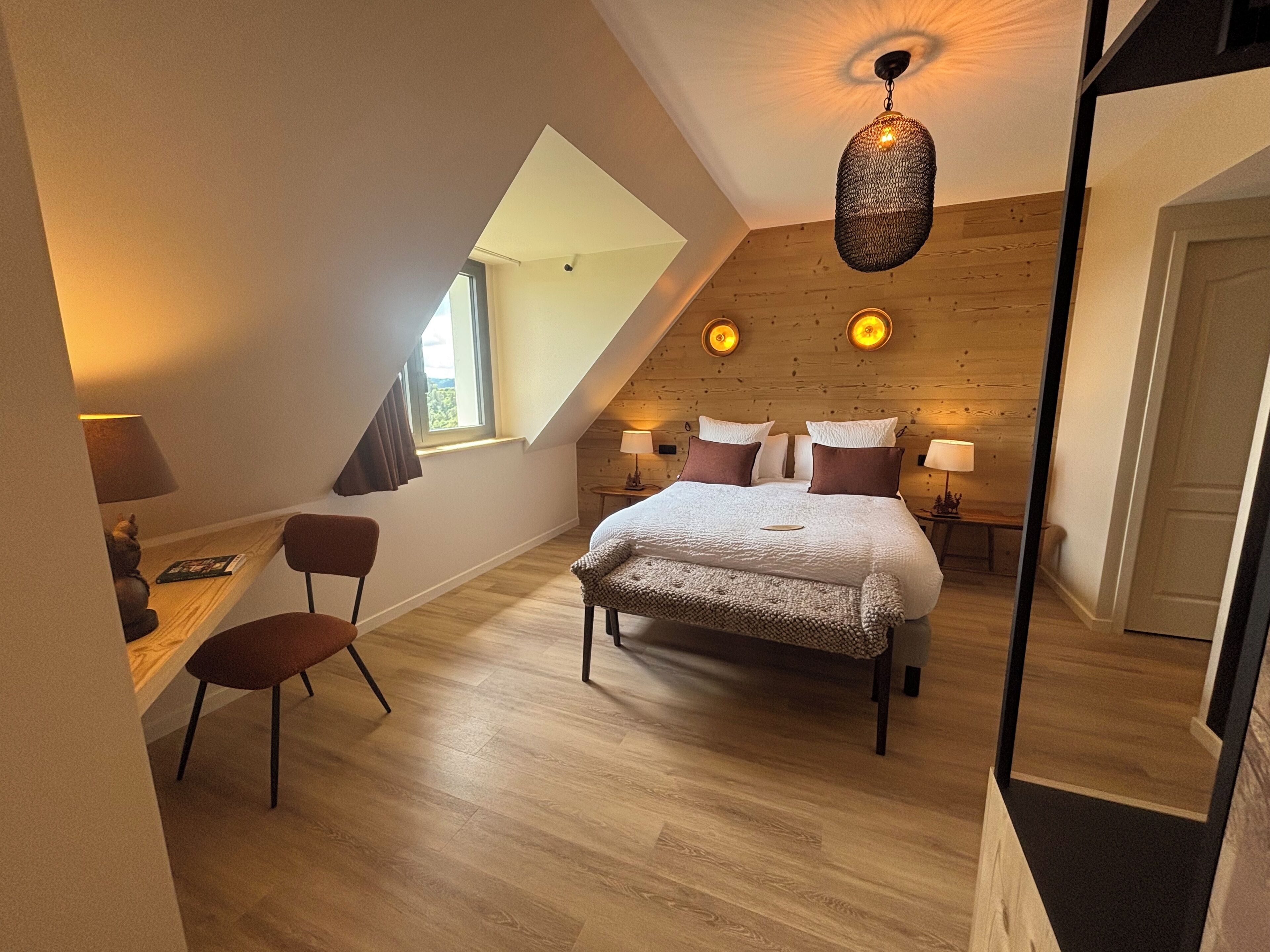 Une chambre avec un plafond en pente, un lit avec des oreillers, une chaise, un bureau et une lampe.