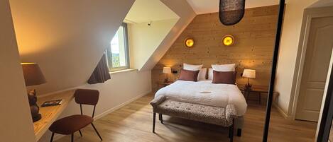 Une chambre avec un plafond en pente, un lit avec des oreillers, une chaise, un bureau et une lampe.