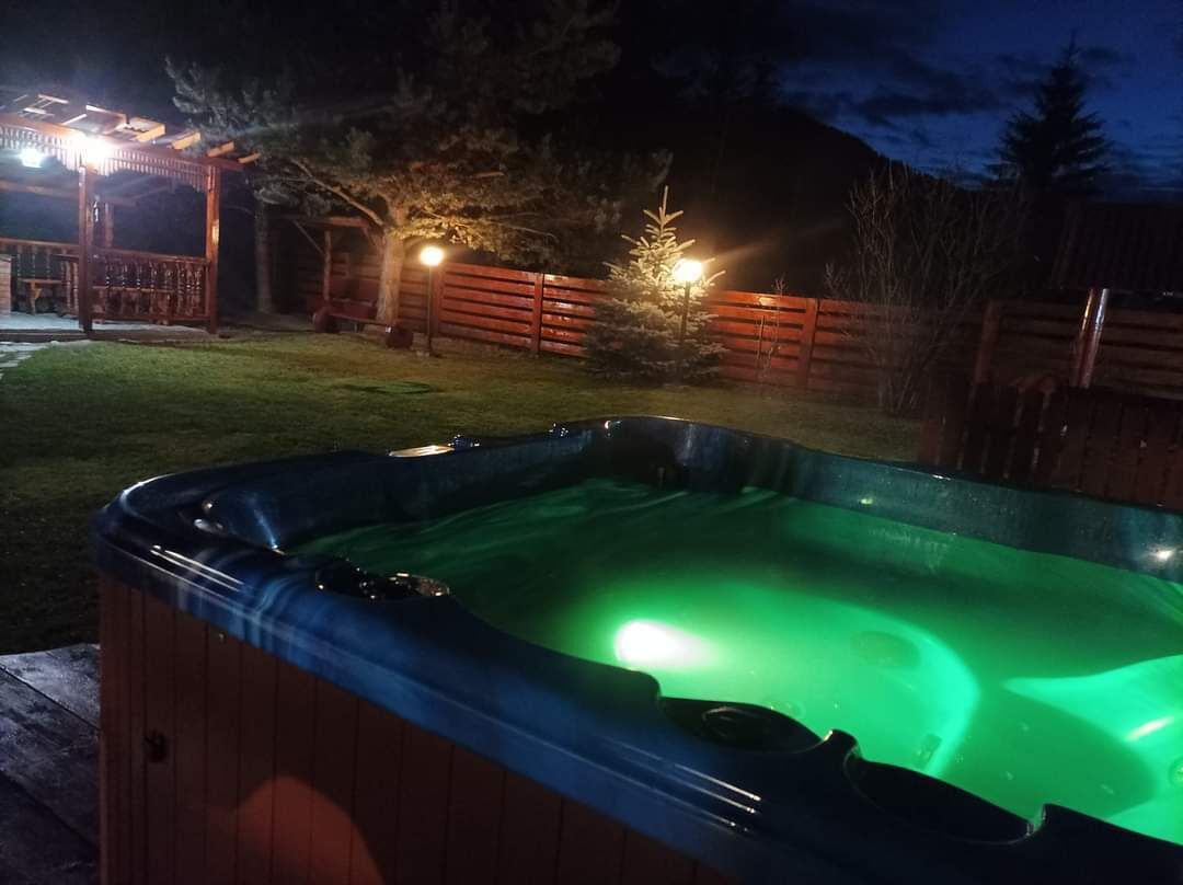 Un jacuzzi en un patio trasero por la noche, con un muelle de madera y cerca de madera.