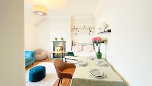 Een gezellige kamer met een bed, een eettafeltje, een blauwe stoel, een blauwe poef en een open haard.
