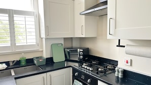 Een moderne keuken met witte kasten, een zwarte kookplaat en een raam met zonwering.