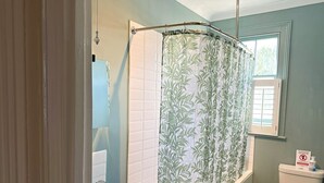 Een badkamer met douchegordijn, toilet, wastafel en raam.