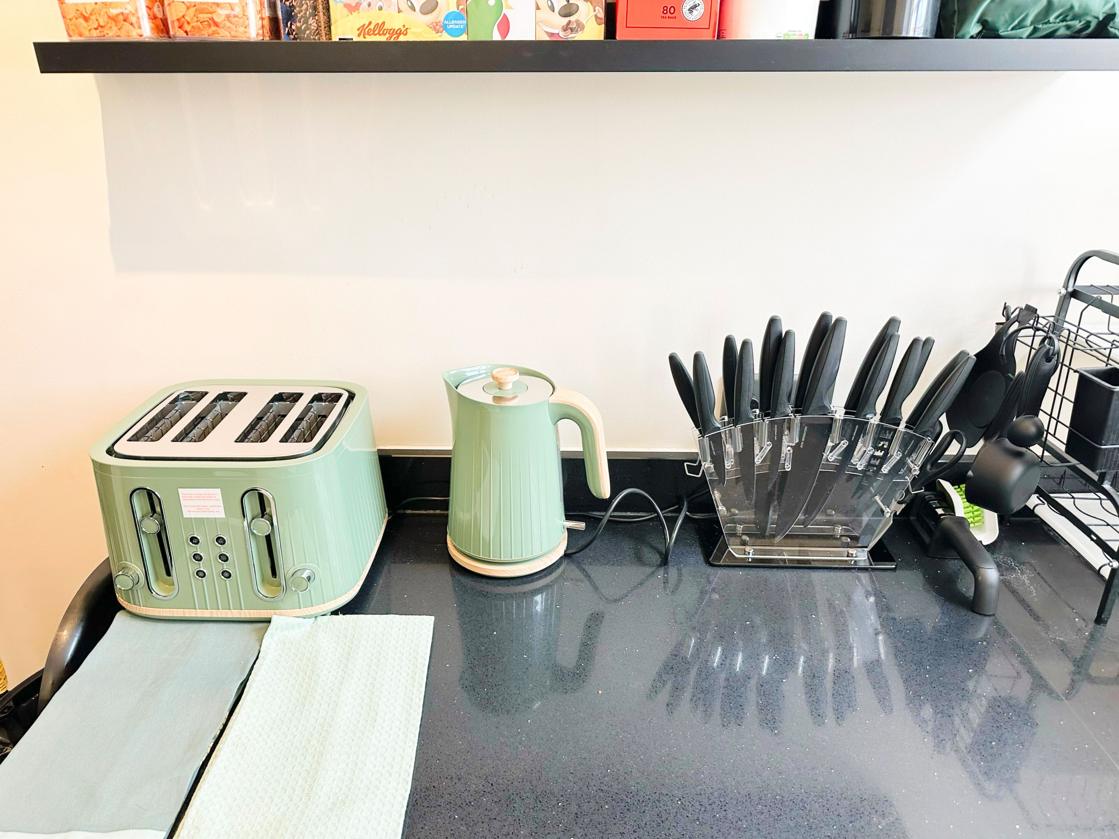 A kitchen counter with a green toaster, a kettle, and a knife holder.