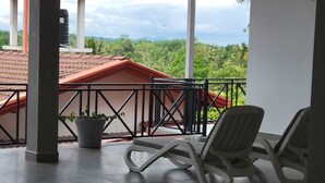 A balcony with two lounge chairs, a potted plant, and a view of a red-roofed building and lush greenery.