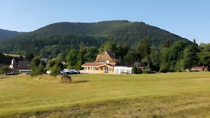 Uma casa com um gramado extenso, uma garagem e uma montanha ao fundo.