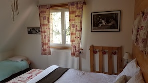 A bedroom with a bed, a window with curtains, a radiator, a wooden headboard, a framed picture, and a bedside table with a lamp.