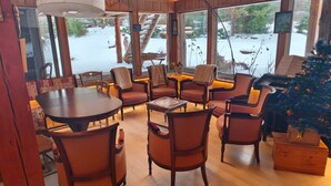A cozy room with a wooden table and chairs, a Christmas tree, and a view of a snowy outdoor area.