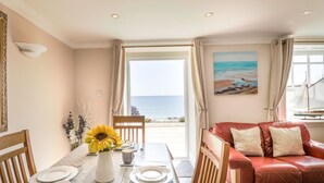 Un comedor con una mesa preparada para dos personas, un sofá de cuero rojo y un cuadro de una playa.