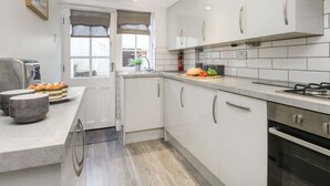 Una cocina moderna con armarios blancos, estufa de acero inoxidable y una encimera con un pan y tomates.