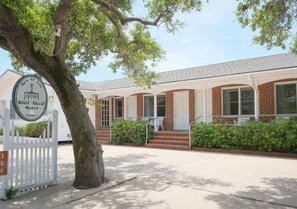 A motel with a white picket fence, a large tree, and a sign indicating it is open all year.