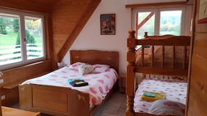 Un dormitorio con dos camas de madera, una ventana con vistas a la vegetación y un cuadro en la pared.