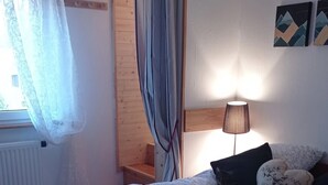Een slaapkamer met een bed, nachtkastje, lamp en raam met gordijnen.