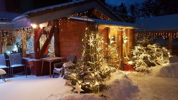 A snow-covered outdoor area with a wooden structure, Christmas lights, and a small table with chairs. - Guest Room 'Chalet Des 3 Pins - Vitamines' with Mountain View, Shared Terrace & Wi-Fi (Plaine)