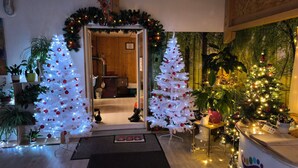 A warmly lit entrance with two white Christmas trees adorned with red ornaments, a wooden interior, and a dining area with a table set for two. - Guest Room 'Chalet Des 3 Pins - Vitamines' with Mountain View, Shared Terrace & Wi-Fi (Plaine)