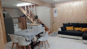 Ein Essbereich mit Tisch und Stühlen, eine Treppe, eine Küchenzeile und ein Sofa mit Kissen.