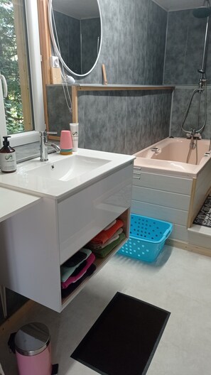 A modern bathroom with a white sink, a mirror, a shower, and a blue laundry basket. - Le Cocon des 3 Pins: Mountain View, Private Terrace & Wi-Fi (Plaine)