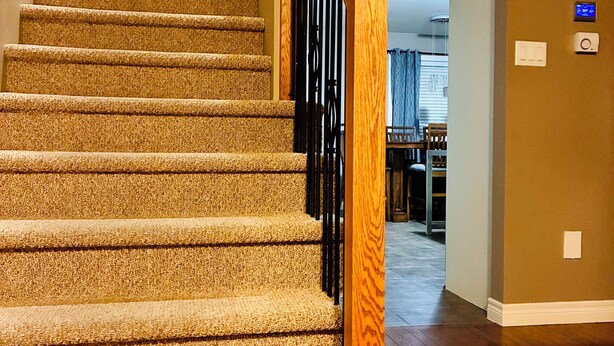 A carpeted staircase with wooden handrails and black metal railings, leading to an upper floor.