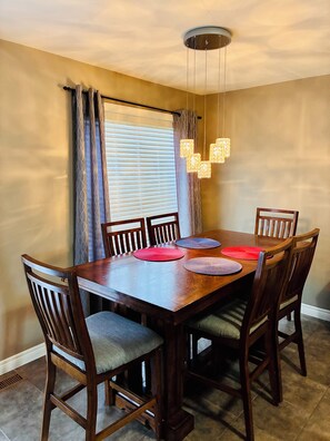 A dining area with a wooden table, chairs, a chandelier, and a window with curtains.