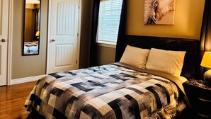 A bedroom with a bed, a window with blinds, a door, and a wall-mounted artwork.