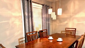 A dining room with a wooden table, four chairs, two white cups with heart designs, and three hanging light fixtures.