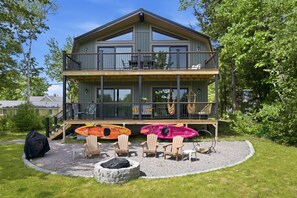 Eine zweistöckige Holzhütte mit Balkon, Sitzgelegenheiten im Freien und Kajaks.