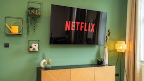 Un salon moderne avec un grand téléviseur à écran plat fixé sur un mur vert, une console en bois agrémentée d’objets décoratifs et un lampadaire.