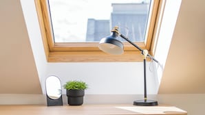 Une lucarne au-dessus d’un bureau, avec une chaise, une lampe de bureau et une petite plante en pot.