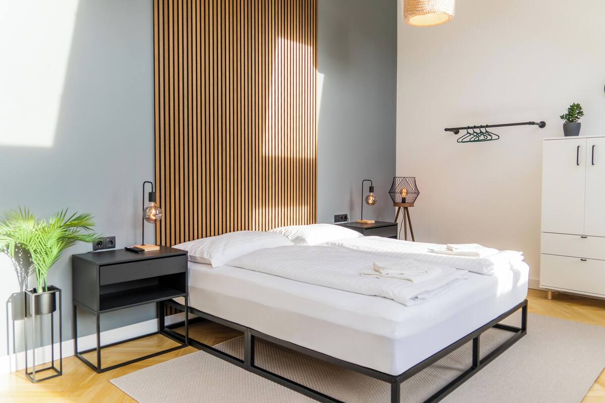 Ein modernes Schlafzimmer mit Bett, Nachttischen, einer Lampe, einem Blumentopf und einem Kleiderschrank.