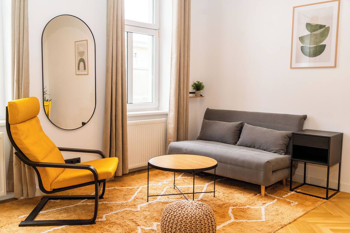 Ein modernes Wohnzimmer mit einer Couch, einem gelben Sessel, einem runden Couchtisch und einem Beistelltisch.