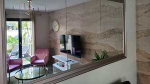 A modern living room with a large mirror, a TV, a pink chair, a glass coffee table, and a clock on the wall. - Prestigious gîte for 24 people - ideal for companies or large groups (Tignieu-Jameyzieu)