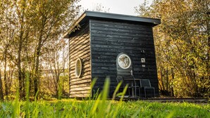 Una petita cabana de fusta amb una finestra circular i una porta, envoltada de verdura.