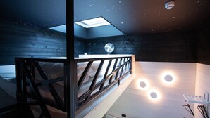 Een slaapkamer met dakraam, een bed met houten hoofdeinde, een ventilator en ronde wandlampen.
