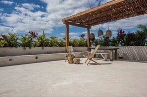 Eine Terrass mit Holz-Pergola, Liegestuhl und Tisch.