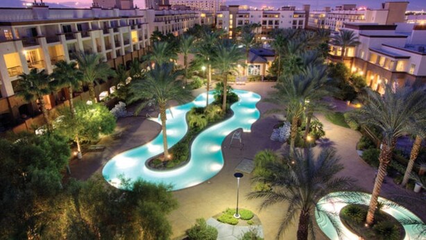 Et resort med en snoet pool, palmer og moderne bygninger.
