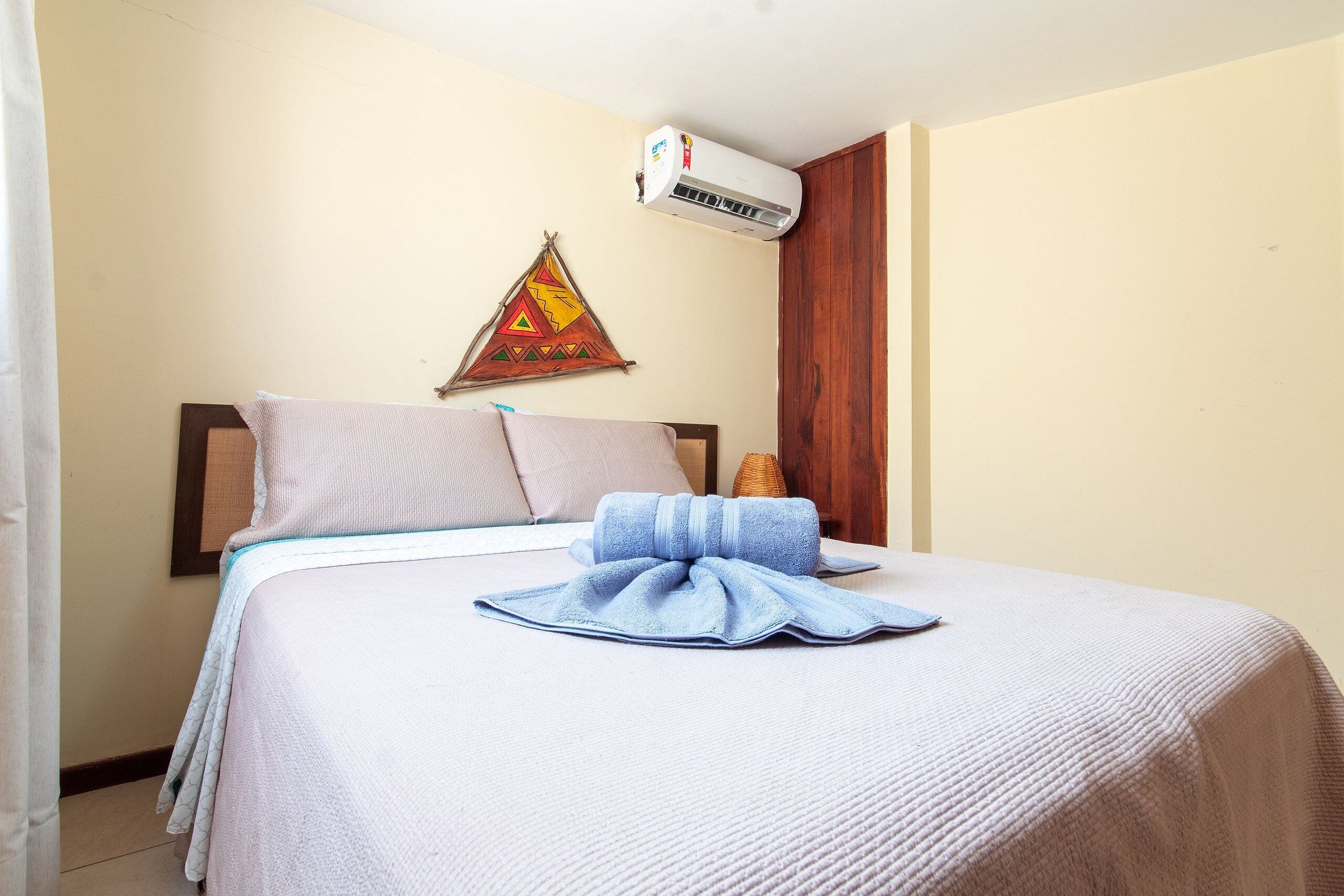 Un lit bien fait, avec une serviette bleue, un climatiseur fixé au mur et une décoration murale.