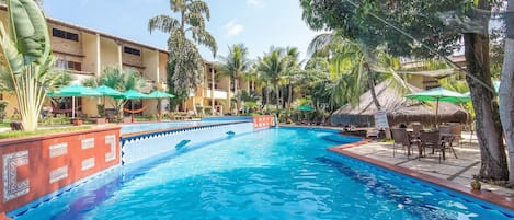 A swimming pool with a tiled edge, surrounded by palm trees and a building with a tiled roof.