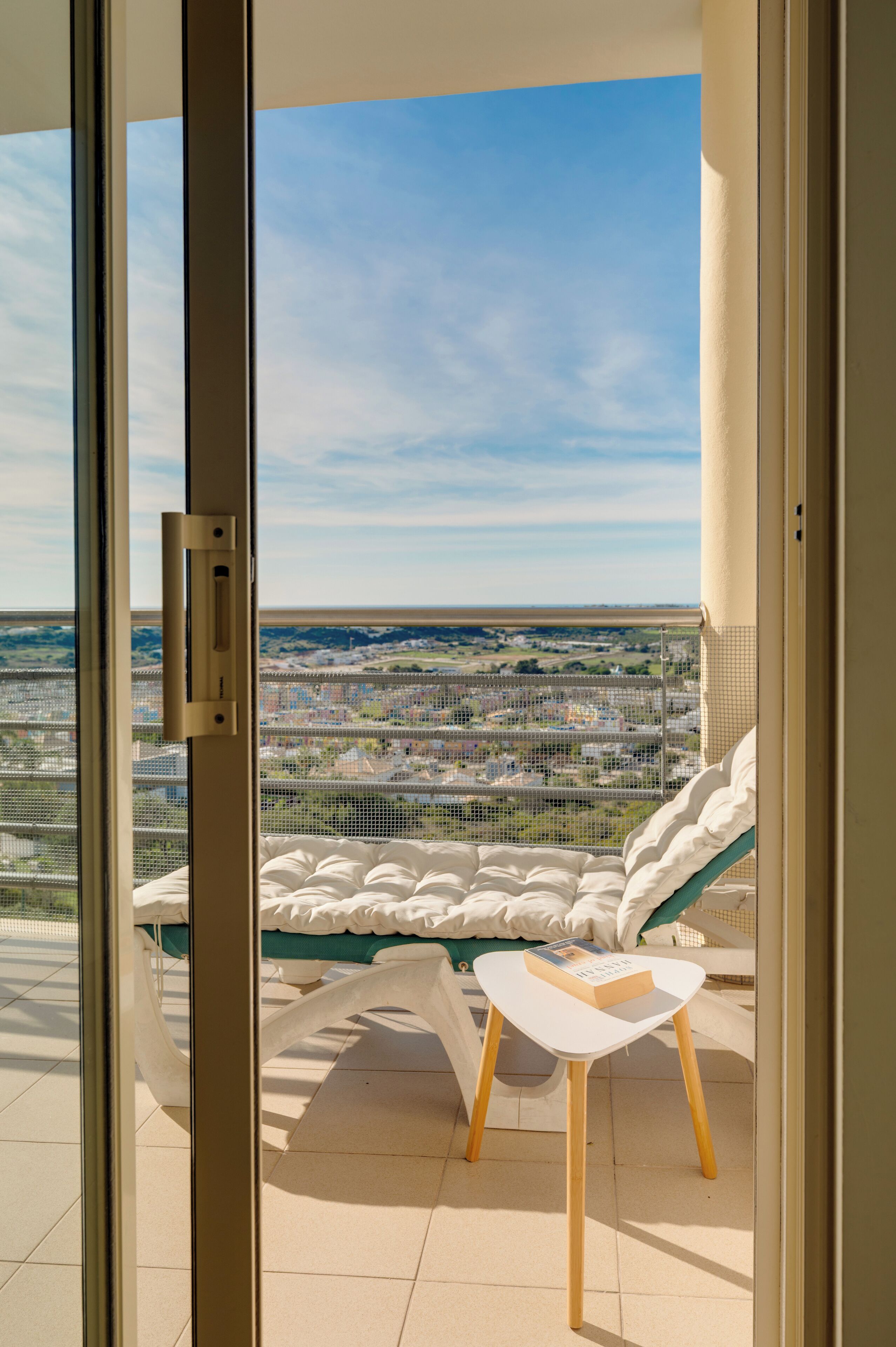 Een balkon met een bed en een tafel, met uitzicht op een stadsbeeld.