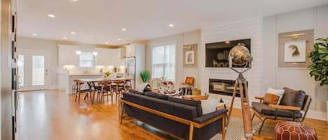 A spacious living area with a sofa, dining table, and chairs. A tripod lamp is positioned near the fireplace.