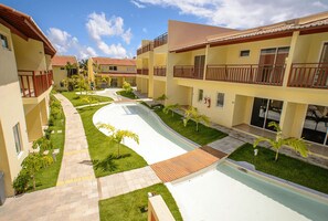 A hotel courtyard with a swimming pool, multiple balconies, and a well-maintained lawn. - Solar Agua Pipa #214 - Flat By Carpediem (Tibau do Sul)