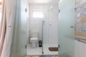 A bathroom with a glass shower enclosure, a toilet, and a small window. - Solar Agua Pipa #214 - Flat By Carpediem (Tibau do Sul)