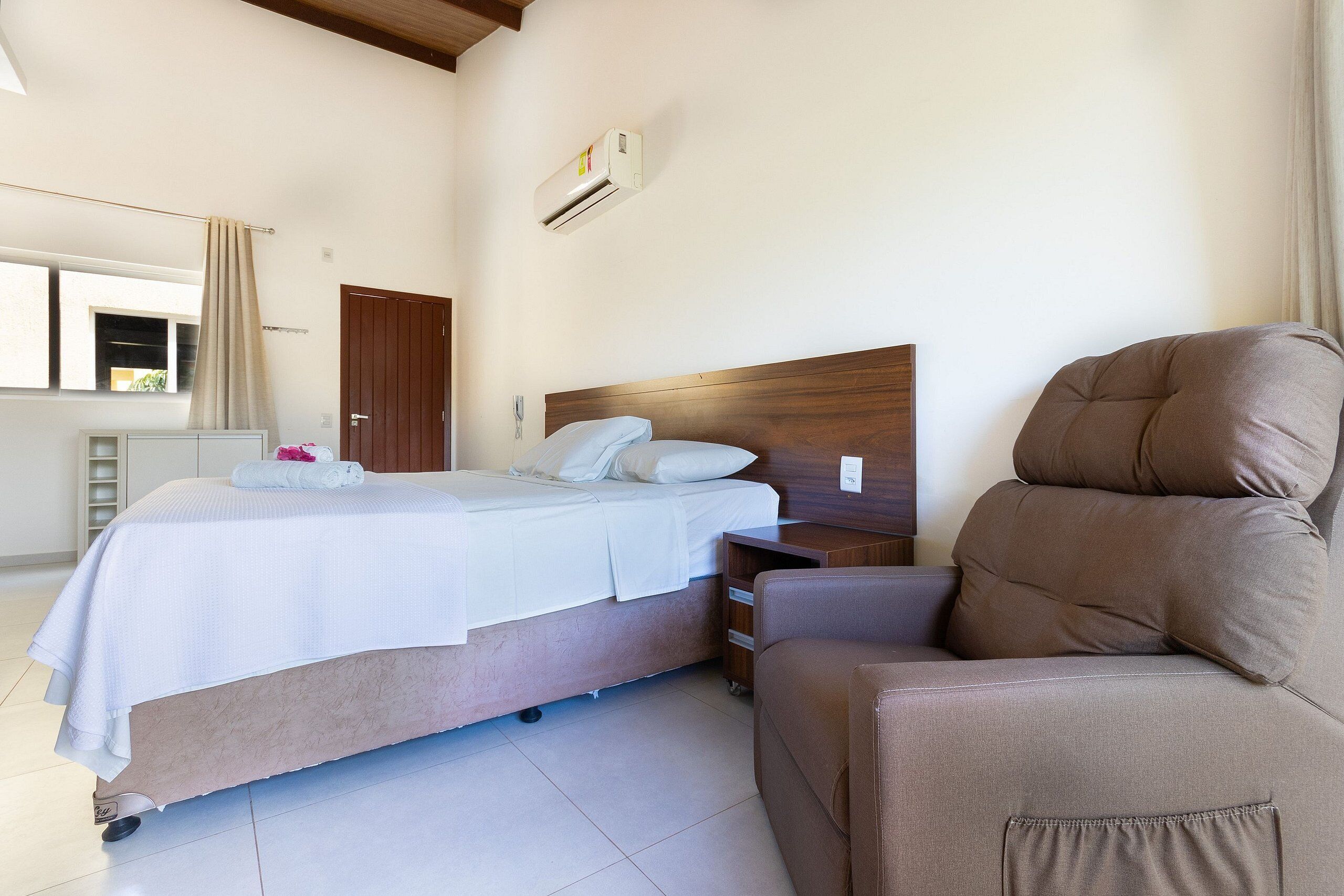 A bedroom with a bed, bedside table, and a brown armchair.
