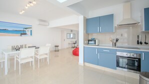 A modern kitchen with blue cabinets, a dining area with white chairs, and a painting on the wall.
