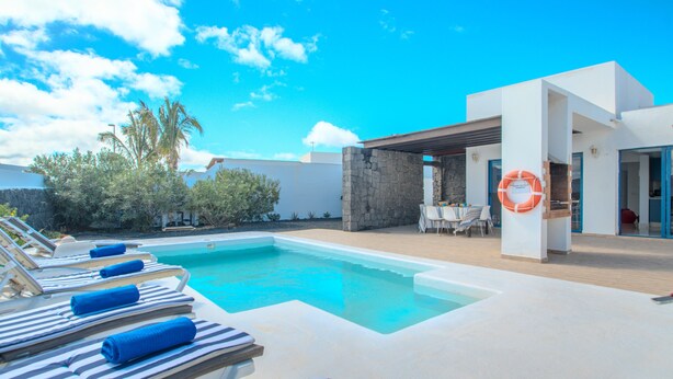 A pool area with lounge chairs and a lifebuoy, surrounded by a modern building with stone pillars.