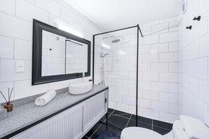 A modern bathroom with a white tiled wall, a large mirror, a white sink, and a glass-enclosed shower. - Bustamante Loft 2D, Metro & Wifi (Providencia)