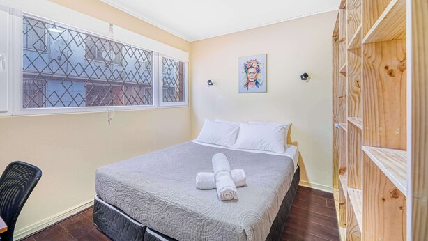 Un dormitorio ordenado con cama, una silla, ventana con vistas y un cuadro en la pared.