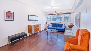Una sala de estar con un sofá azul, una mesa de centro de vidrio, un banco de madera y un sillón rojo.